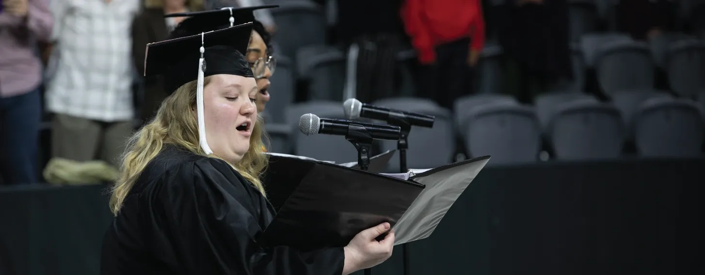 Student singing in cap and gown at graduation.